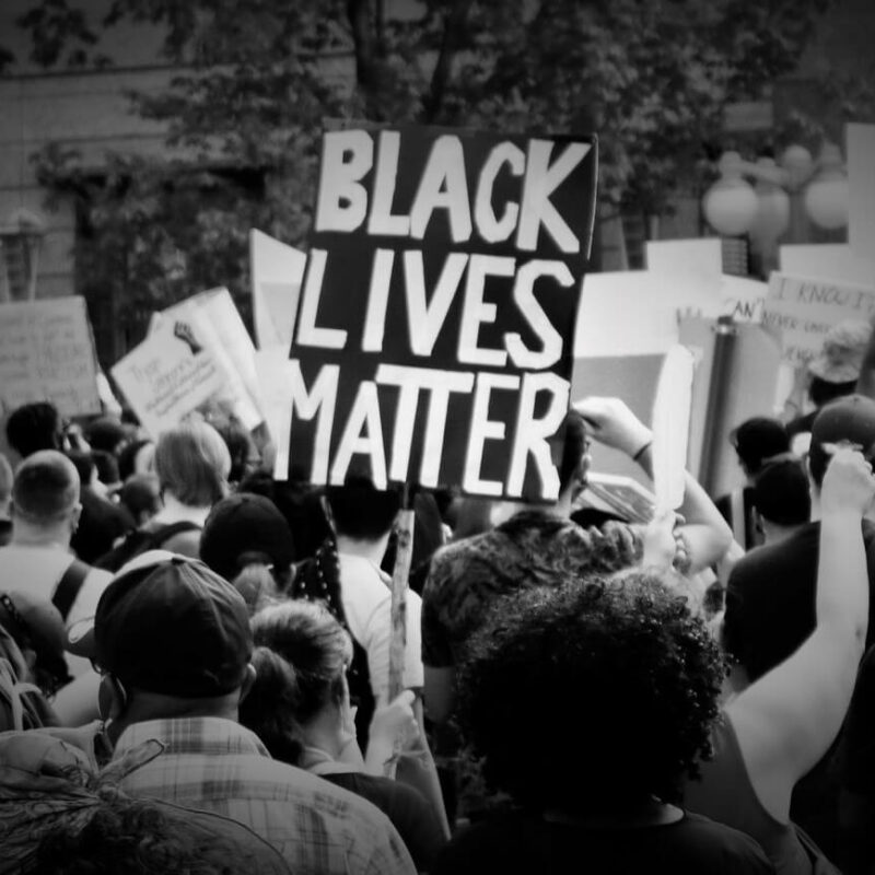 Black and White photo from BLM protest with sign displaying "Black Lives Matter"
